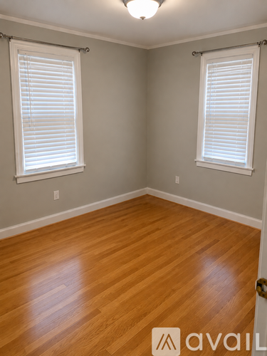 A room with wooden floors and two windows with blinds.