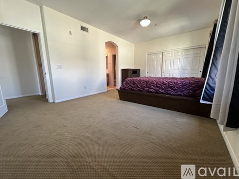 A bedroom with a purple bedspread and a brown carpet.