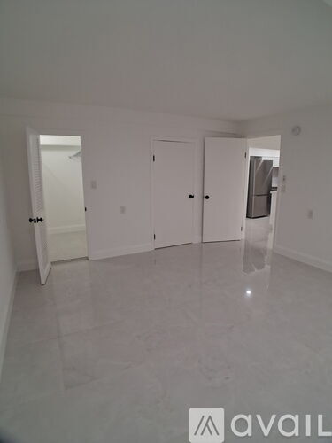 A spacious room with white walls and flooring, and a door on the left side.