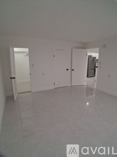 A spacious room with white walls and flooring, and a door on the left side.