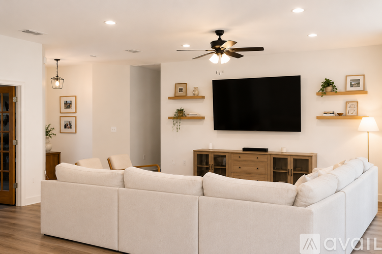 A living room with a white couch and a flat screen TV mounted on the wall.