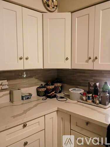 A kitchen with white cabinets and a countertop with various items on it.