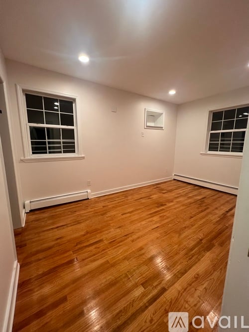 A room with wooden flooring and two windows.