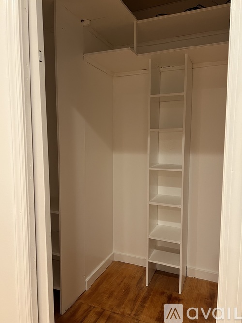 A white shelving unit with multiple shelves is in a room with wooden flooring.