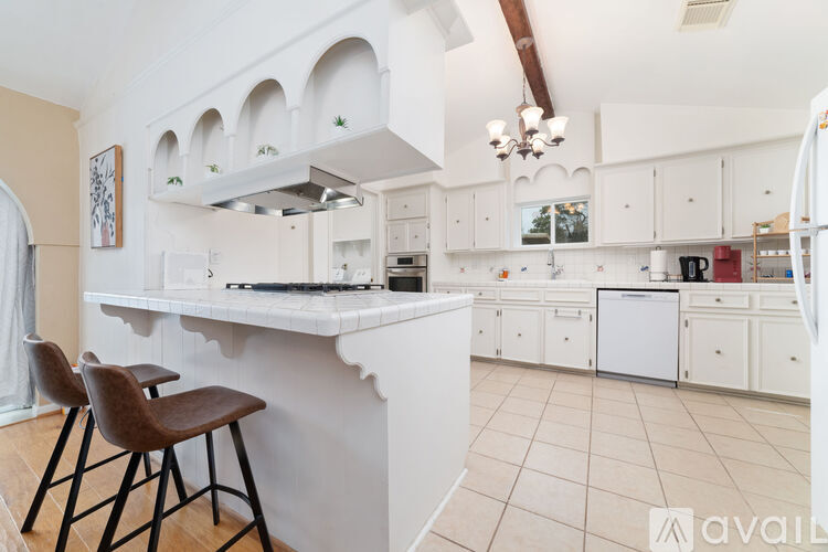 A kitchen with white cabinets and a large island with a bar stool in front.