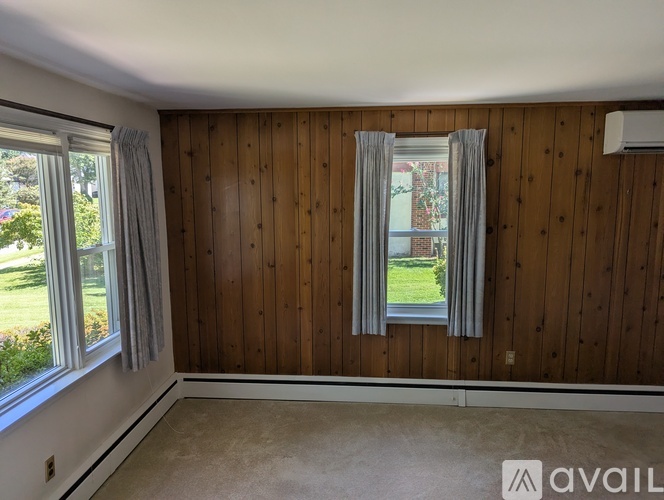 A room with wooden walls and a window with a view of a lawn and trees.