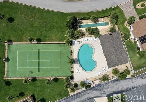 A tennis court is surrounded by a pool and a grassy area.