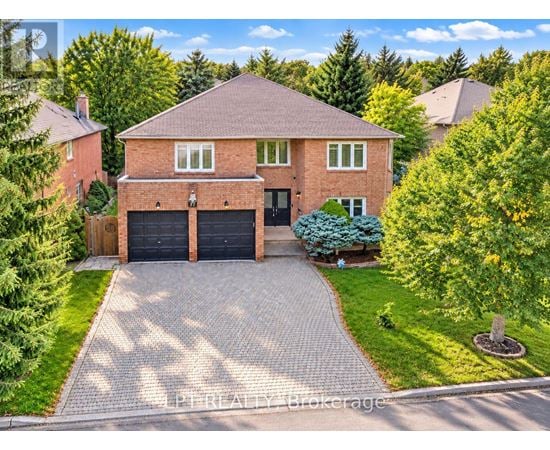 A house with a brick facade and a black garage door is surrounded by greenery.