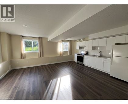 A well-lit, empty kitchen and living room with wood flooring and white cabinetry.