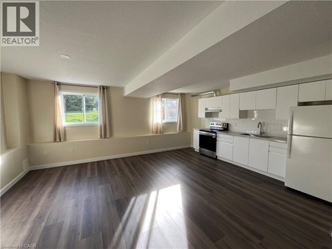 A well-lit, empty kitchen and living room with wood flooring and white cabinetry.