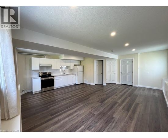 A well-lit, spacious room with wood flooring and a kitchen area in the background.
