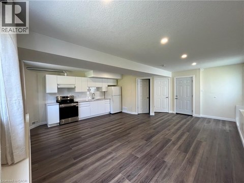 A well-lit, spacious room with wood flooring and a kitchen area in the background.