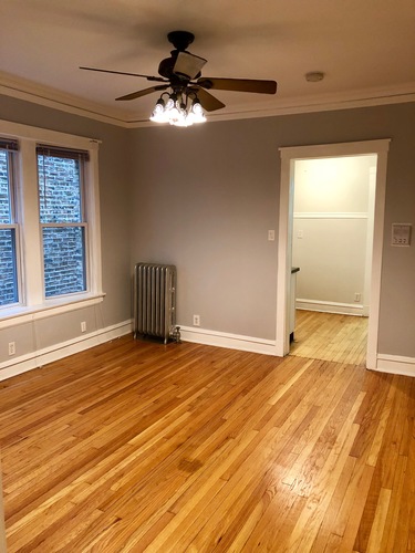 A room with a ceiling fan and wood flooring.