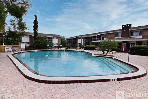A swimming pool surrounded by a brick patio and apartment buildings.