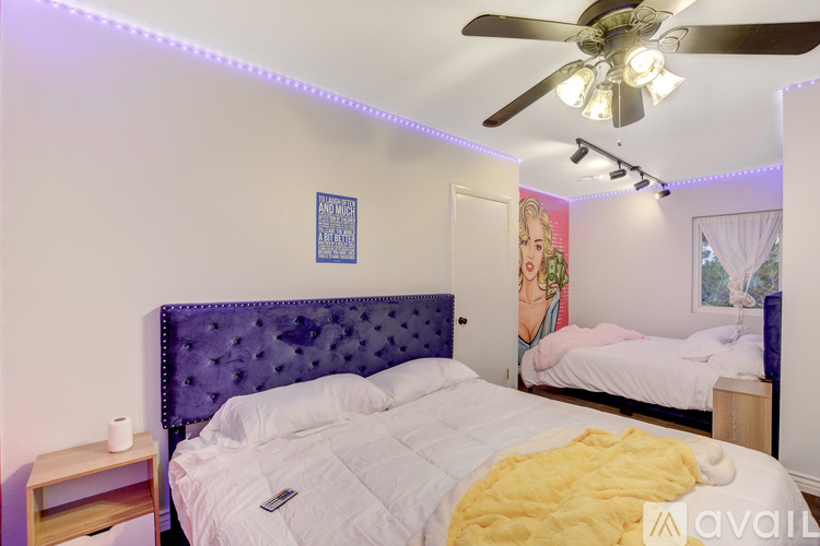 A bedroom with a purple headboard bed and a white bed in the background.