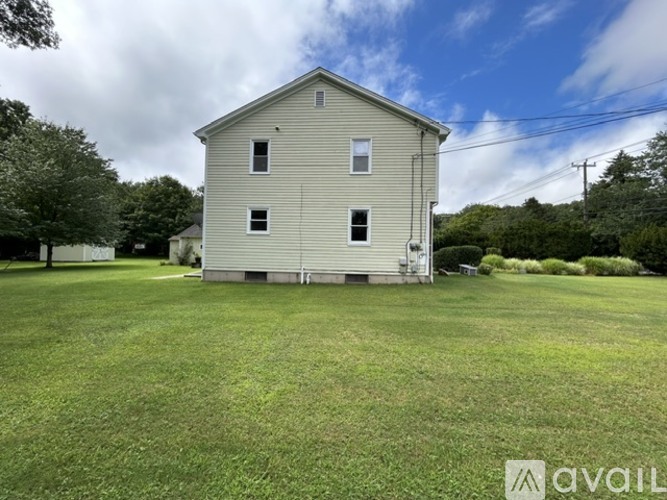 A two-story house with a grey exterior and a white door is surrounded by a grassy lawn.