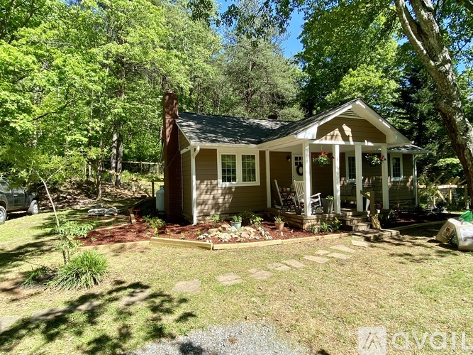A house with a porch and a covered patio is surrounded by trees.