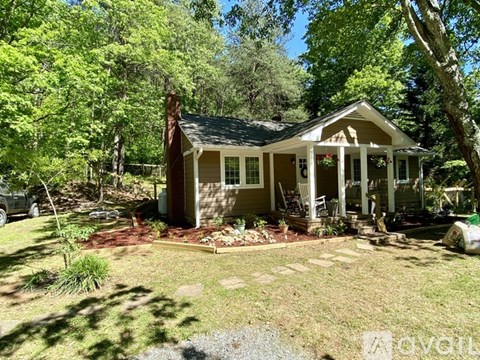 A house with a porch and a covered patio is surrounded by trees.