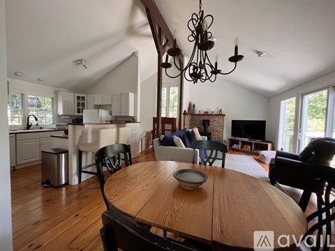 A wooden dining table with chairs and a chandelier hangs in a spacious living room.