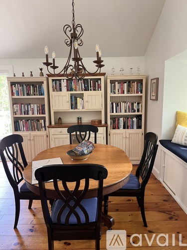 A dining room with a round table and chairs, a chandelier, and bookshelves.