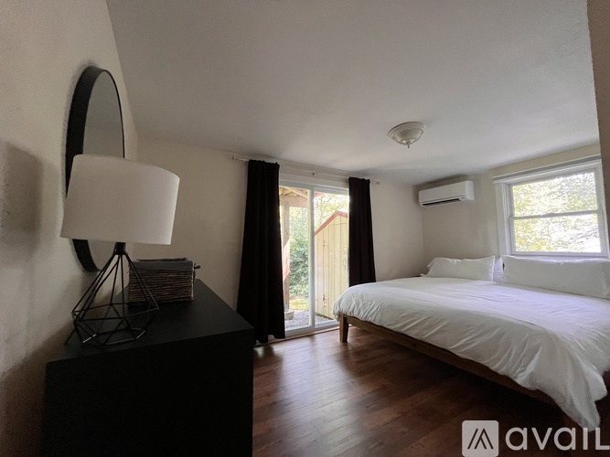 A bedroom with a white bed and a black dresser with a lamp on top.