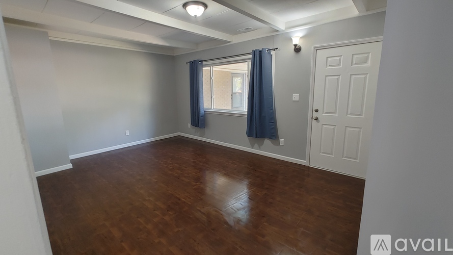A room with wooden flooring and a window with blue curtains.