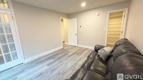 A living room with a black leather couch and a wooden floor.