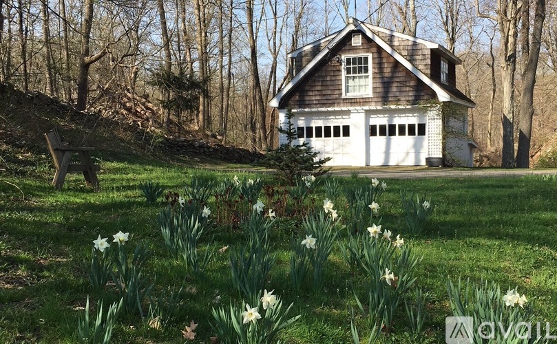 A house with a white garage door is surrounded by a grassy field with daffodils.