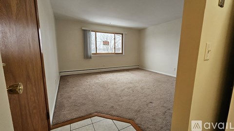 A room with a carpeted floor, a window, and a door.