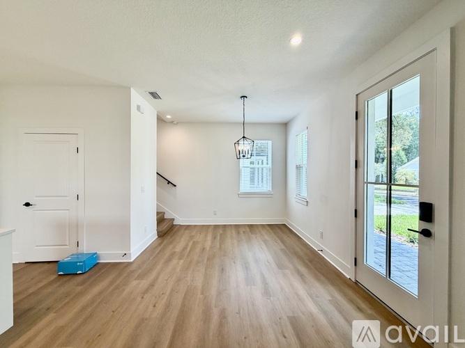 A room with wooden floors and white walls, a chandelier hanging from the ceiling, and a door leading outside.