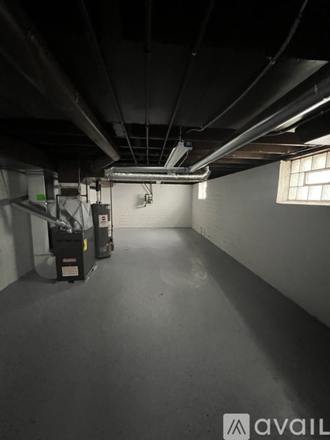 A spacious, empty basement with concrete floors and walls, featuring a large window on the right side.