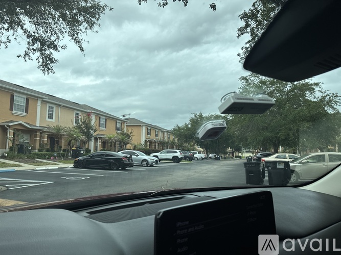 A car is driving through a residential area with houses on the left and parked cars on the right.