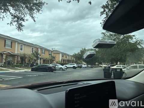 A car is driving through a residential area with houses on the left and parked cars on the right.