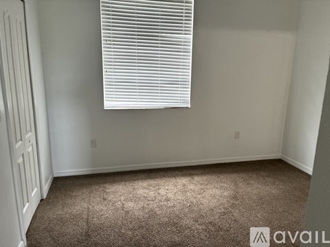 A room with a carpeted floor and a window with blinds.