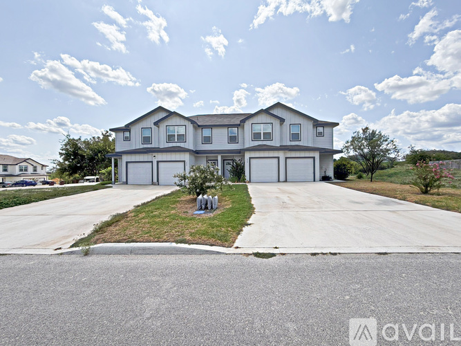 A large, modern house with a grey roof and white walls is surrounded by a well-maintained lawn and a clear sky.