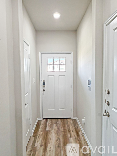 A hallway with a white door and wooden flooring.
