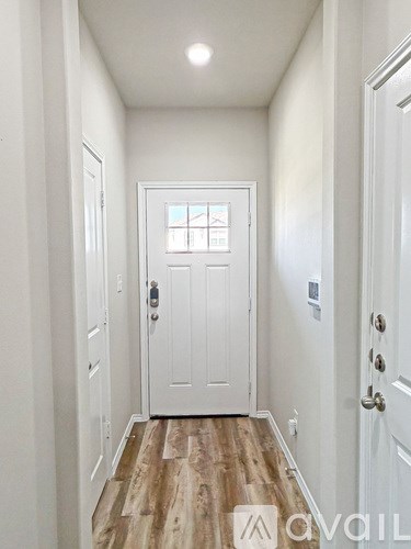 A hallway with a white door and wooden flooring.