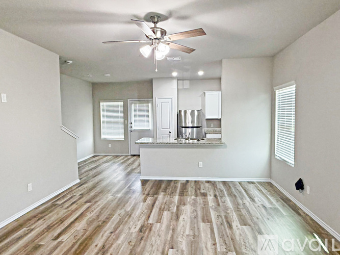 A spacious kitchen and living room with wood flooring and white walls.