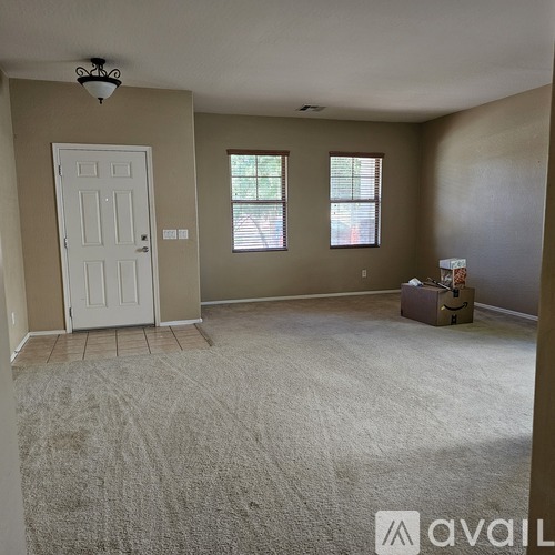 A room with a white door and two windows with a box on the floor.