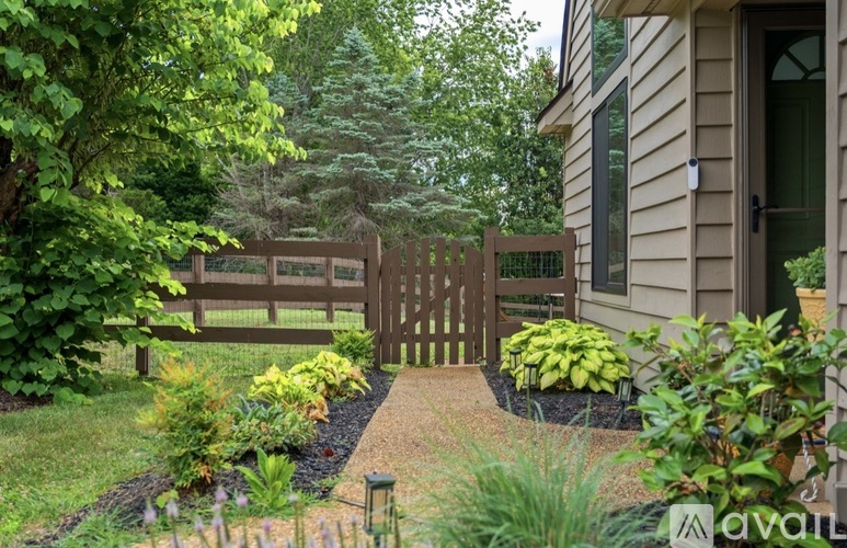 A wooden gate leads to a house surrounded by greenery.