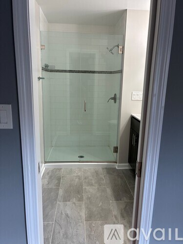 A bathroom with a glass shower door and grey tiled floor.