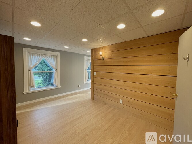 A room with wooden walls and a window with a view of trees.