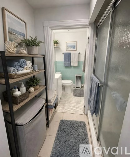 A bathroom with a toilet, a shower, and a shelf with towels and plants.