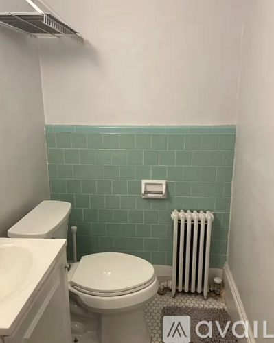 A white toilet sits in a bathroom with a green tiled wall.