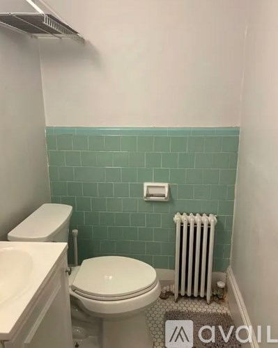 A white toilet sits in a bathroom with a green tiled wall.