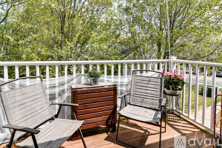 Two chairs and a table on a balcony with trees in the background.