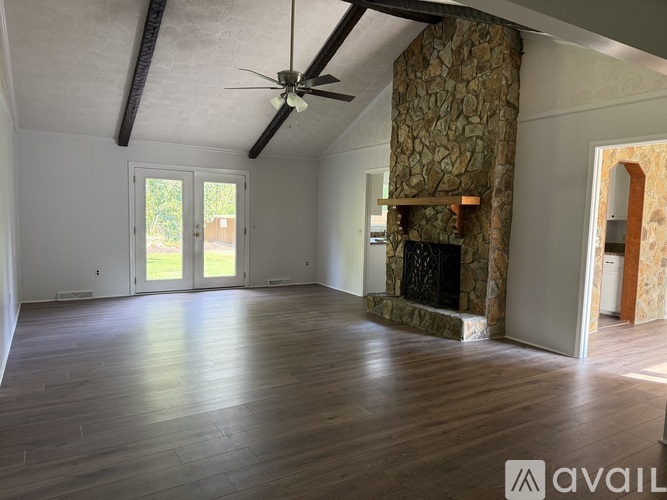 A spacious room with a stone fireplace and wood flooring.