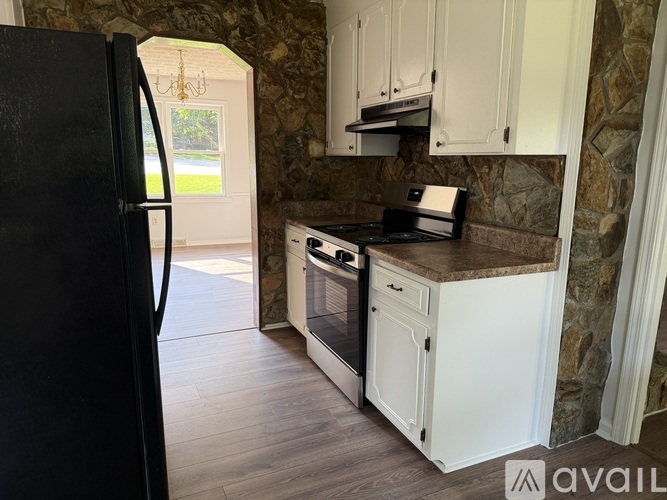 A black refrigerator stands in a kitchen with white cabinets and a stone backsplash.