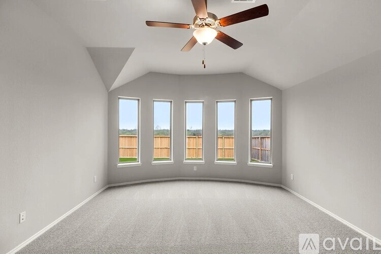 A spacious room with a ceiling fan and large windows overlooking a fence.