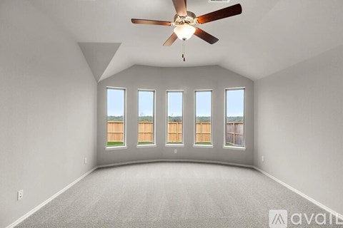 A spacious room with a ceiling fan and large windows overlooking a fence.